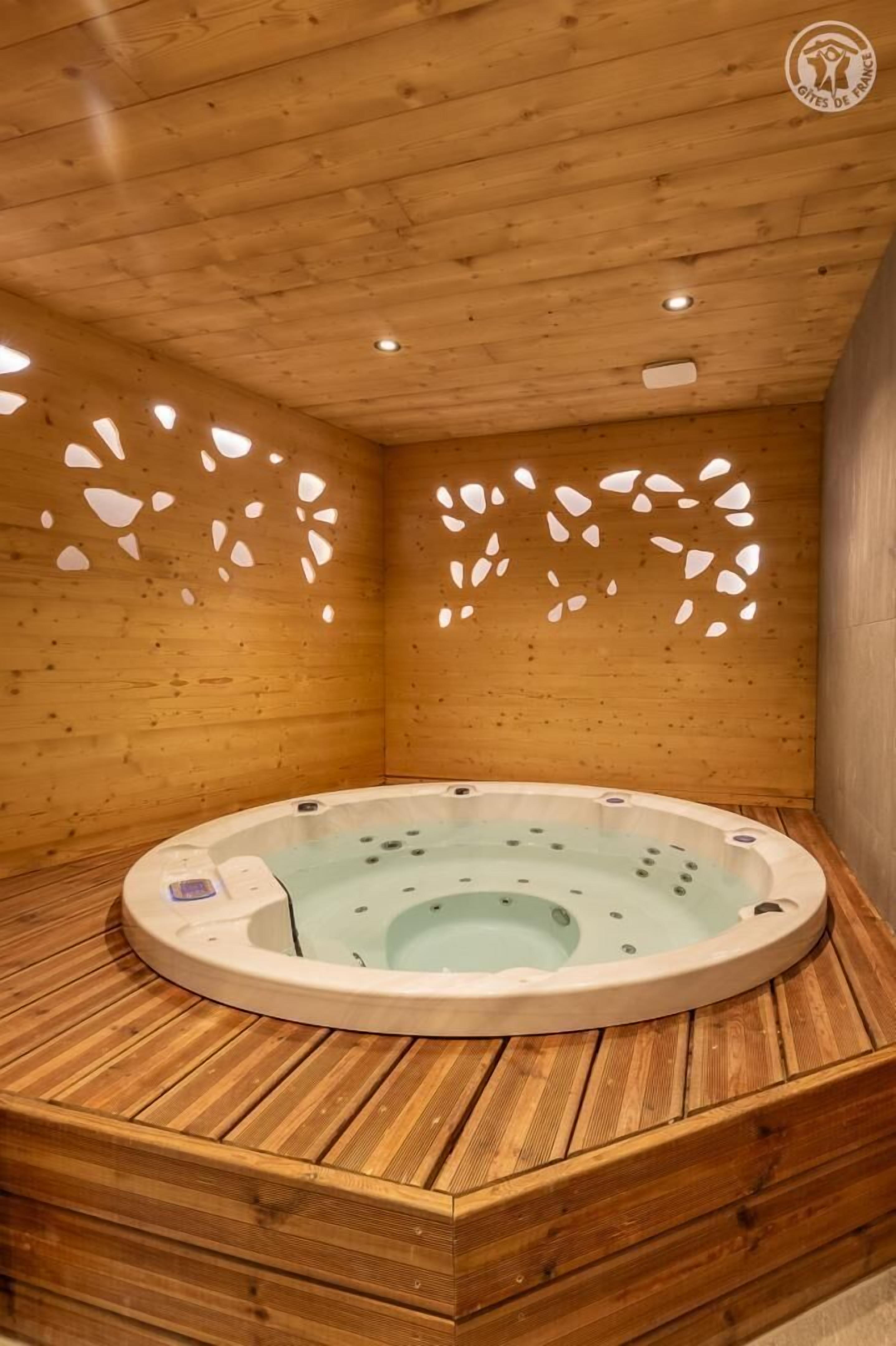 Una sauna de madera con un jacuzzi circular, paredes de madera y un techo inclinado con iluminación empotrada.
