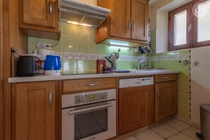 Cocina con armarios de madera, horno empotrado, lavavajillas y encimera con diversos utensilios de cocina.