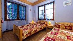 A room with two wooden beds, each with a quilted bedspread, a radiator, and two windows with blue curtains. - LA CASCADE - LA GIETTAZ (LA GIETTAZ)