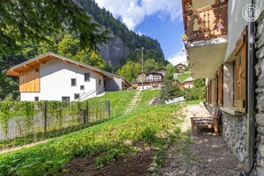 Una zona residencial en una ladera con una casa blanca, un muro de piedra y un balcón de madera.