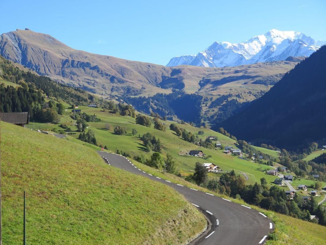 Une route sinueuse qui traverse un paysage montagneux, avec des maisons et un ciel dégagé.