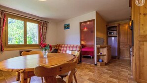 A cozy room with a wooden dining table, a sofa, and a bed. There is a window with curtains, a small painting on the wall, and a kitchenette with a refrigerator. - LE REPOSU - BEAUFORT ARECHES (BEAUFORT ARECHES)