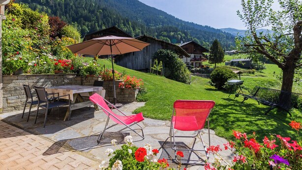 A patio with a table and chairs, surrounded by flowers and a view of a mountain. - LE REPOSU - BEAUFORT ARECHES (BEAUFORT ARECHES)