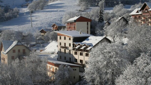 Un pueblo cubierto de nieve con edificios tradicionales de madera, un telesilla al fondo y una vista despejada del paisaje nevado circundante.