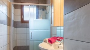 Un baño moderno con cabina de ducha de vidrio, un lavamanos con toalla roja y muebles de madera.