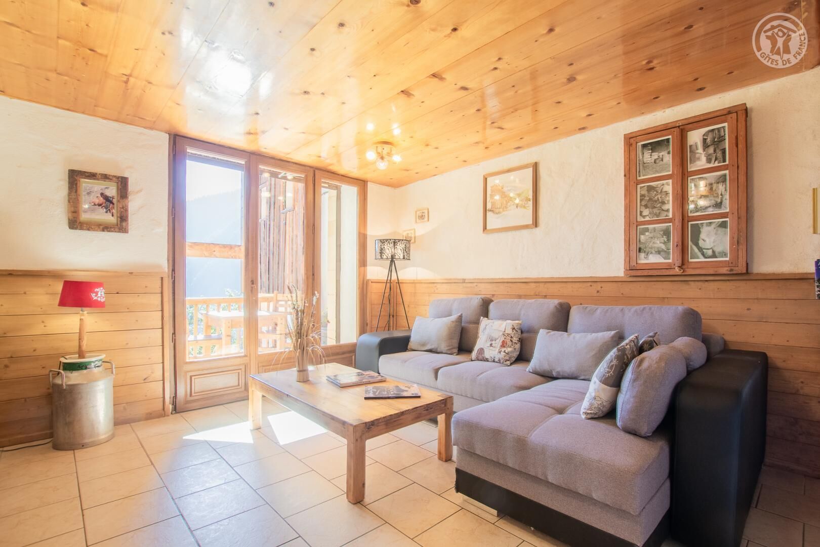 Un salon chaleureux avec un canapé, une table basse et une lampe. Les murs sont ornés de tableaux encadrés et une fenêtre offre une vue agréable.