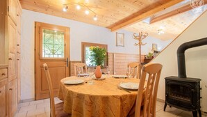 Una sala da pranzo con un tavolo rotondo apparecchiato per quattro persone, sedie di legno, un vaso con fiori e un camino a legna nero.