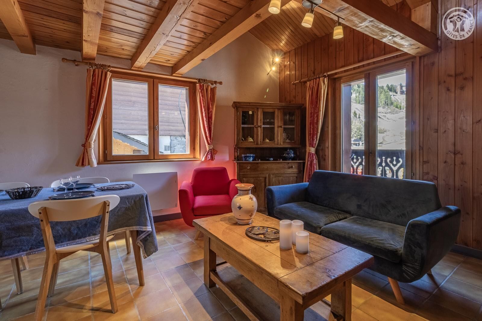 Une pièce chaleureuse avec un plafond en bois, une table à manger avec des chaises, un canapé et un buffet aux portes vitrées.