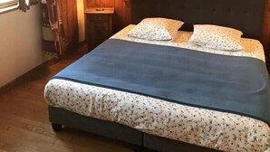 A bedroom with wooden panel walls, a bed with floral bedding, a nightstand with a lamp, and a window with curtains. - FLORINEIGE - COURCHEVEL (COURCHEVEL)