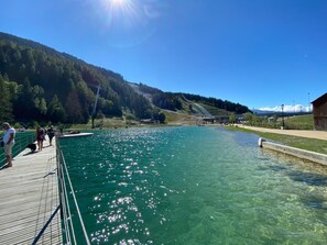 Un lago transparente con un muelle de madera y un edificio pequeño al fondo.