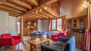 A spacious living area with wooden beams, a dining table, red and blue chairs, and a kitchen with wooden cabinets. - FLORINEIGE - COURCHEVEL (COURCHEVEL)