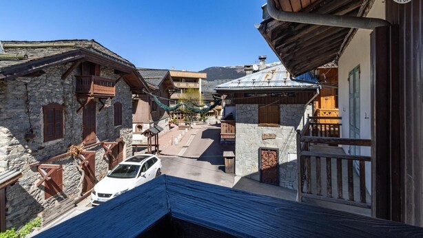 A narrow street with stone buildings, a white car parked on the side, and a wooden balcony overlooking the street. - FLORINEIGE - COURCHEVEL (COURCHEVEL)