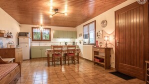 A cozy kitchen with wooden ceiling, a dining table with chairs, a refrigerator, and a microwave.