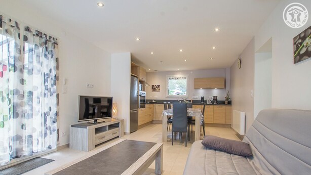 A modern living room with a sofa, TV, and a dining area with a table and chairs. - LES LILAS - LA BIOLLE (LA BIOLLE)