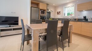 A modern kitchen with a dining table, chairs, a refrigerator, oven, microwave, and a TV. - LES LILAS - LA BIOLLE (LA BIOLLE)
