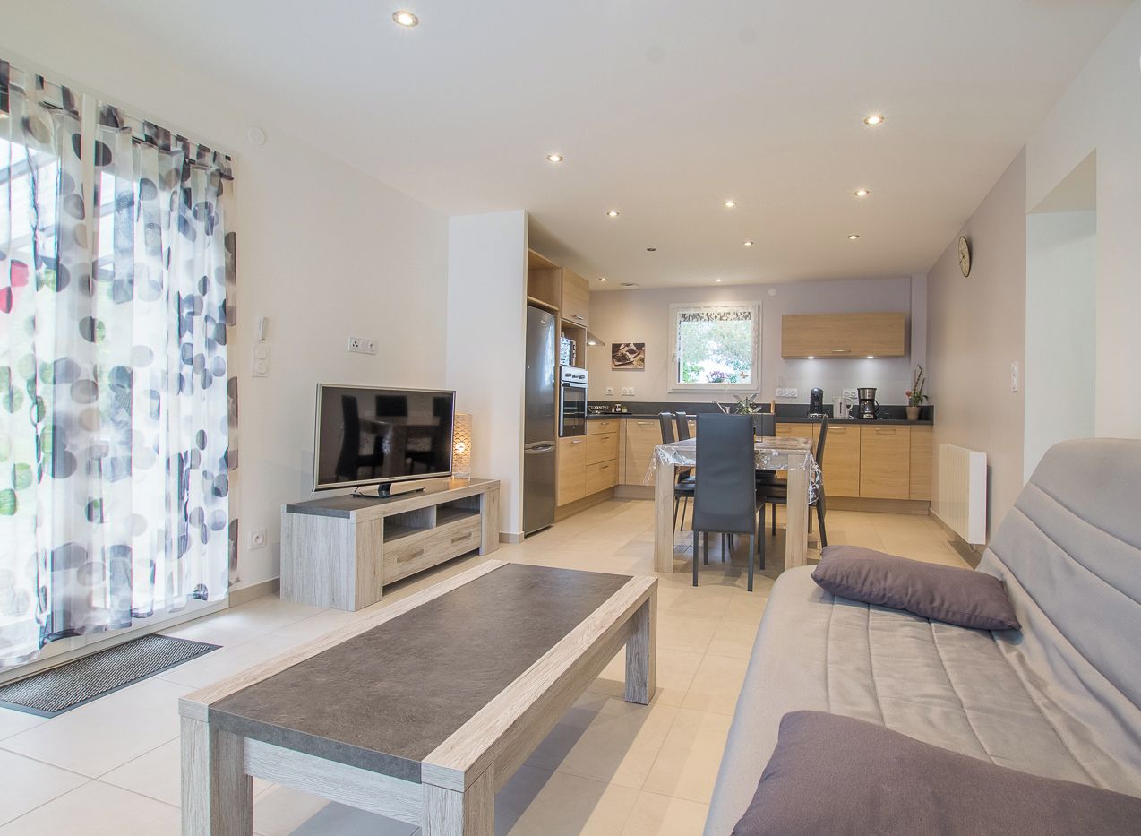 Een moderne woonkamer met een bank, televisie en een eethoek met tafel en stoelen.