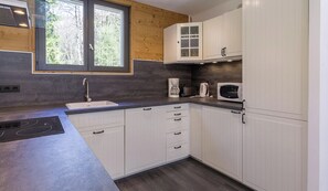 Una cocina moderna con armarios blancos, microondas integrado y cafetera.