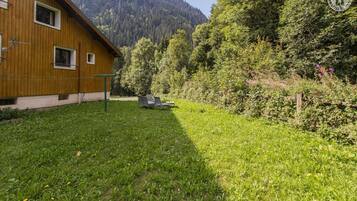 Une cabane en bois avec une cour verdoyante et une chaîne de montagnes en arrière-plan.