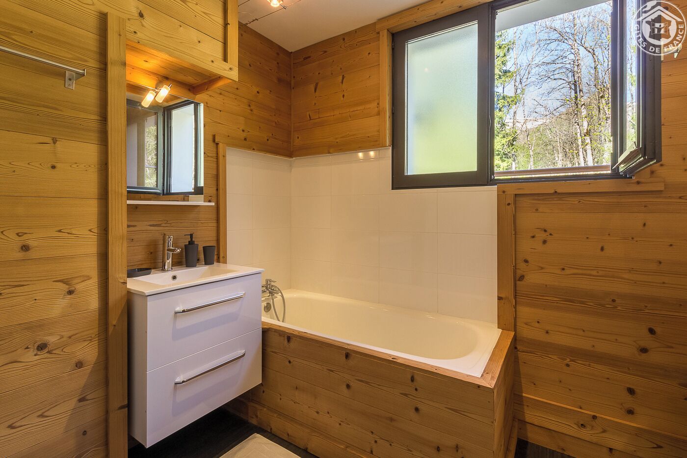 Une salle de bain rustique, avec des murs en bois, un lavabo blanc, un miroir et une baignoire.
