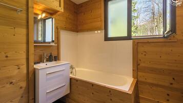 Une salle de bain rustique, avec des murs en bois, un lavabo blanc, un miroir et une baignoire.