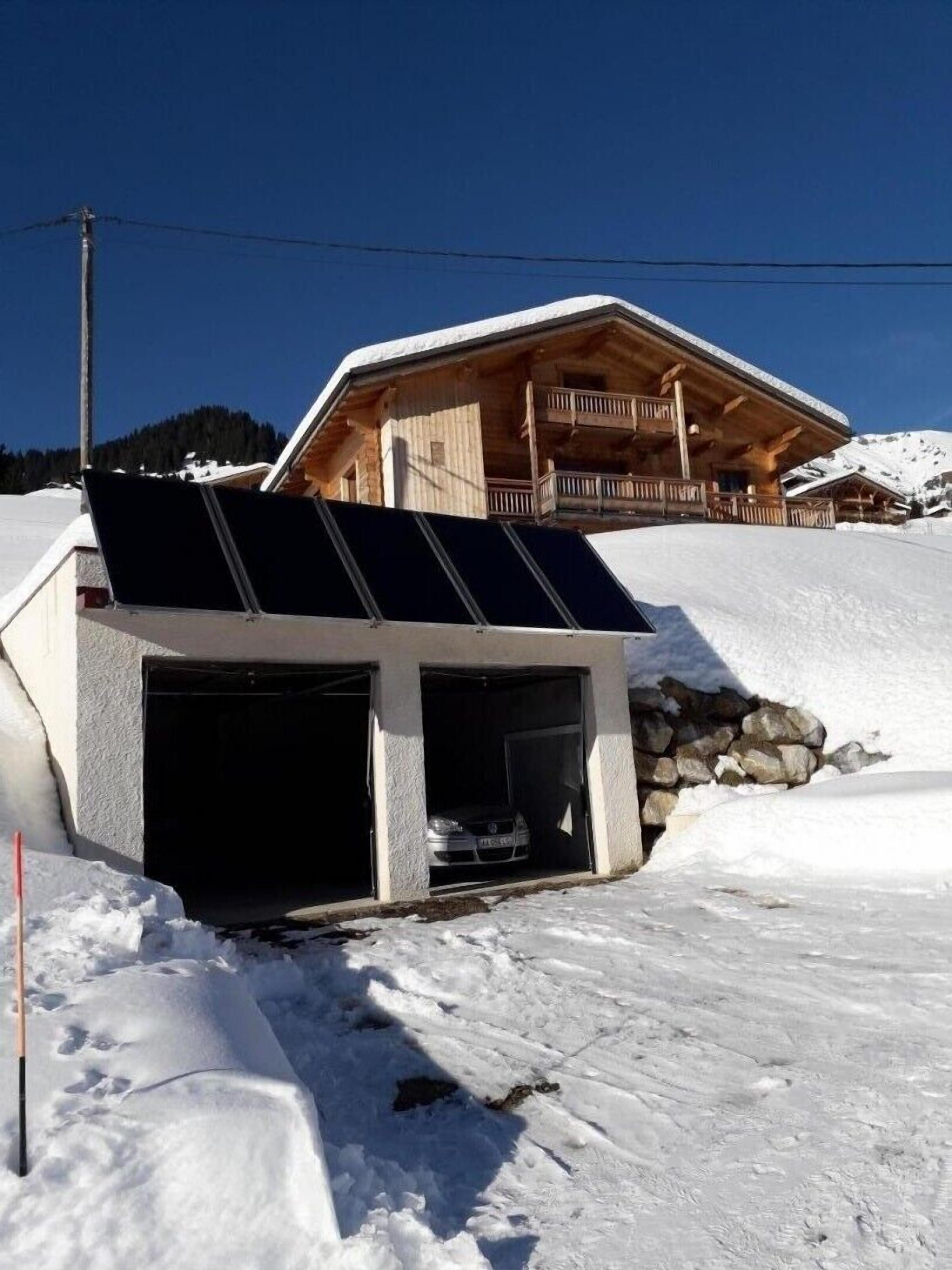 A wooden chalet with a balcony, a garage, and solar panels on the roof.