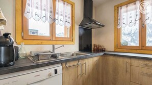 A kitchen with wooden cabinets, a black range hood, a Bosch dishwasher, and a window with a curtain featuring reindeer designs. - CHALET FIASSE - HAUTELUCE LES SAISIES (HAUTELUCE LES SAISIES)