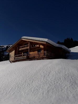 Situated on a snow-covered slope, this chalet offers a traditional alpine view from its balcony.