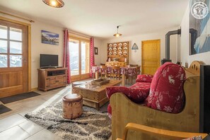 Relax in this inviting living room with a view of the snowy landscape, featuring a comfortable armchair and a dining area.