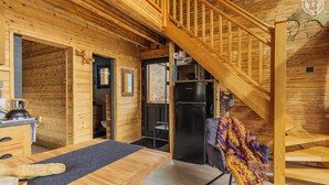 Interno di una baita in legno con angolo cottura, un tavolo da pranzo, un frigorifero nero e una scala.