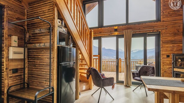 Un accogliente interno di una baita, con arredamento in legno, un'area pranzo e vista sulle montagne.