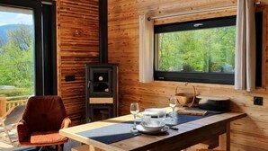 Un interno in legno con un tavolo da pranzo apparecchiato per due, un camino e vista su una foresta attraverso una finestra.