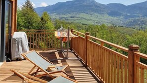 Una terrazza in legno con poltrone relax e un'amaca, con vista su un paesaggio montuoso.