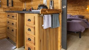 Interno di una baita in legno con angolo cottura, dotato di pensili, un piano di lavoro e un bollitore.