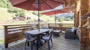 A wooden deck with a table and chairs, an umbrella, and a view of a mountainous landscape.