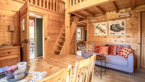 A wooden cabin interior with a dining area, a sofa, and a staircase.