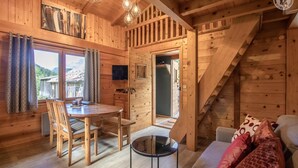 A wooden cabin interior with a dining area, a sofa, and a staircase.
