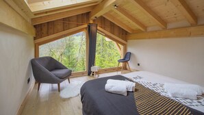 Un dormitorio con una ventana grande, una cama, una silla y un taburete pequeño.