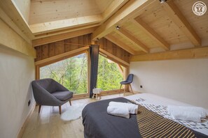 Quarto com uma janela grande, cama, cadeira e um banquinho.