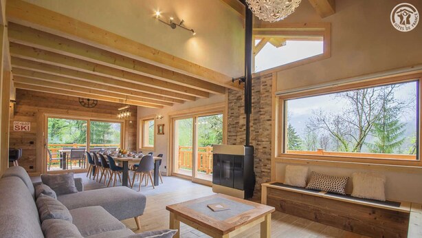 Una sala de estar acogedora con chimenea, un comedor y grandes ventanales con vistas al exterior.