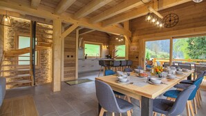 Interior de una cabaña de madera con comedor, cocina y una escalera.
