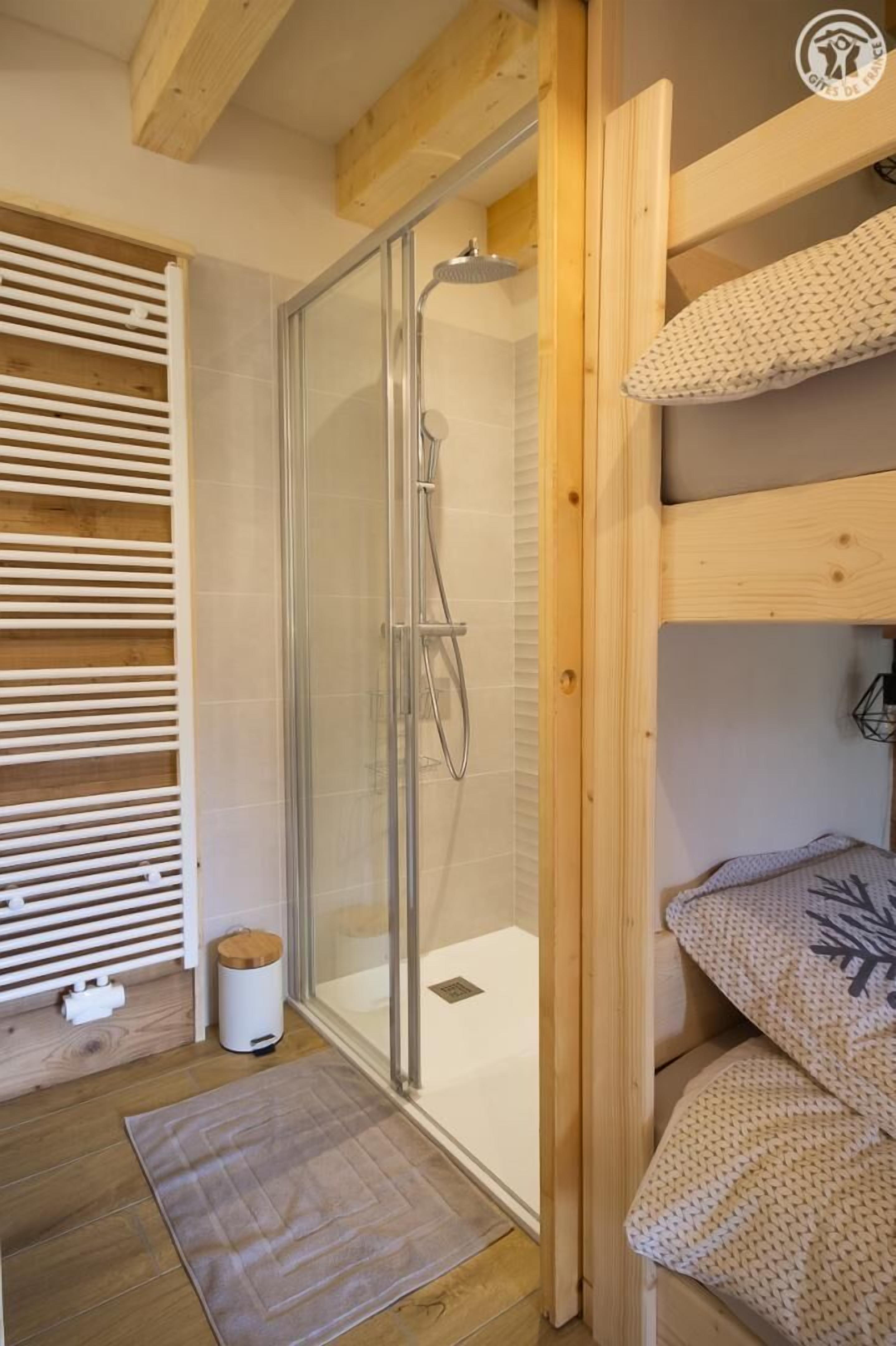 Interior em madeira com box de vidro, radiador branco e beliche com almofadas estampadas.