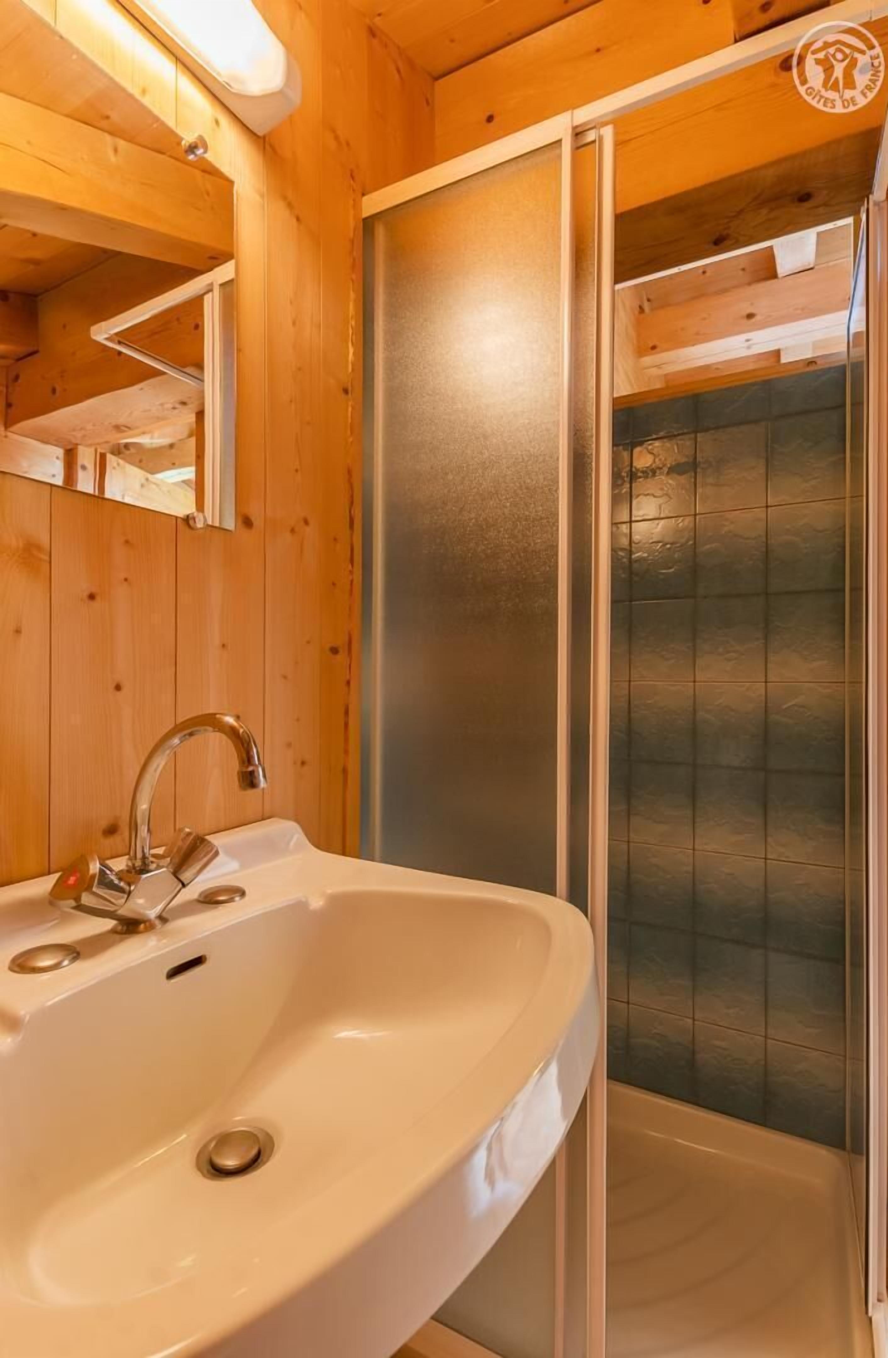 Een houten badkamer met een witte wastafel, een spiegel en een douchecabine.