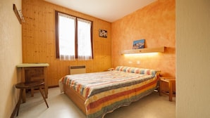 Ein Zimmer mit Holzboden, einem Bett mit gestreifter Decke, einem Schreibtisch mit Stuhl und einem Fenster mit Vorhängen.