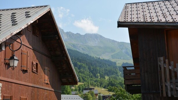 Ein hölzernes Gebäude mit geneigtem Dach, einer sichtbaren Treppe und einer Berglanschaft im Hintergrund.
