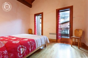 A bedroom with a bed, a wooden chair, a window with a view of a house, and a door. - LES PELEVES - VALMOREL LES AVANCHERS (VALMOREL LES AVANCHERS)