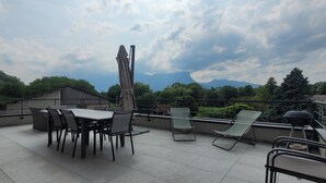 A rooftop terrace with a table and chairs, a barbecue grill, and a view of mountains and trees. - L'OREE DU LAC - LES MOLLETTES (LES MOLLETTES)