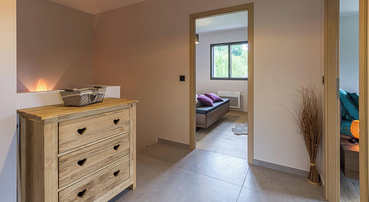 A modern interior with a wooden dresser, a sofa, and a view through an open doorway to a room with a window.