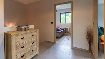 A modern interior with a wooden dresser, a sofa, and a view through an open doorway to a room with a window.