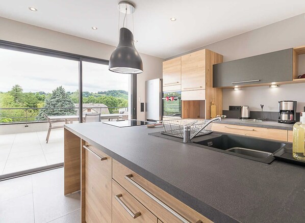 A modern kitchen with a large island, a built-in oven, and a view of the outdoors.