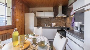 A compact kitchen with wooden walls, a dining table with a floral tablecloth, and modern appliances. - CHALET DES CIMES - NOTRE DAME DU PRE (NOTRE DAME DU PRE)